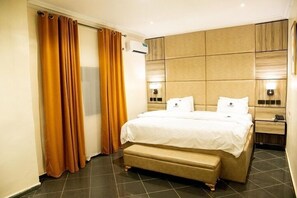 A hotel room with a large bed, a bench, a wardrobe, and a nightstand with a lamp. - Lamonde Bysomwhere (Jos)