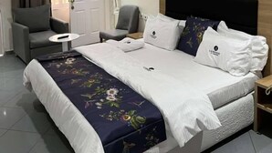 Habitació d'hotel amb un llit gran, dues butaques, una taula petita i una cambrera de nit.