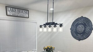 Un coin repas avec une table en bois foncé, des chaises blanches, un banc, un luminaire suspendu et une assiette décorative posée sur la table.