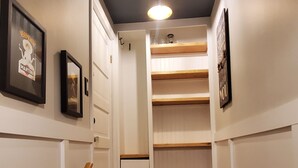 Un corridoio stretto con pavimento in legno, pareti bianche e una scala in legno che conduce a una zona mansardata.