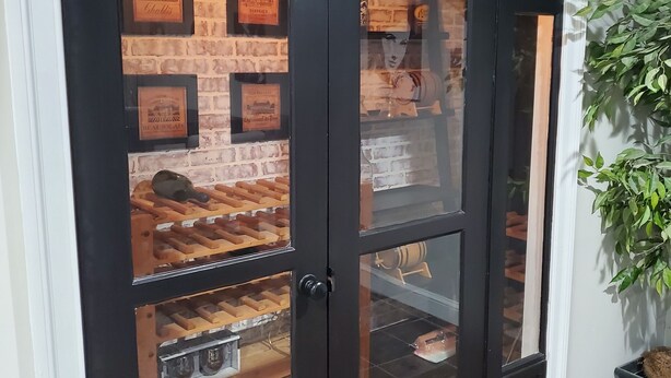 Una porta in vetro con cornice nera e scaffali multipli che espongono bottiglie di vino e certificati incorniciati.