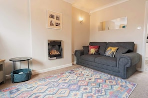 A living room with a sofa, a patterned rug, a fireplace, and a small table with a basket. - Great home by Chester Greenway, EV Charger (Chester)