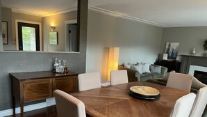 A dining area with a wooden table and chairs, a kitchen area with a wooden cabinet, and a living room with a sofa and fireplace. - Tranquil setting with beautiful views overlooking Skaha Lake  (Okanagan Falls)