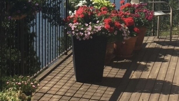 A wooden deck with potted flowers and a table with chairs, overlooking a body of water and mountains. - Tranquil setting with beautiful views overlooking Skaha Lake  (Okanagan Falls)