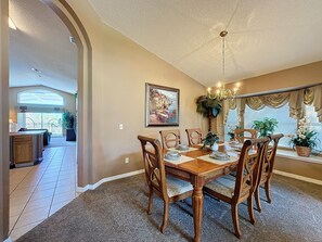 A dining room with a large wooden table, six chairs, and a chandelier.