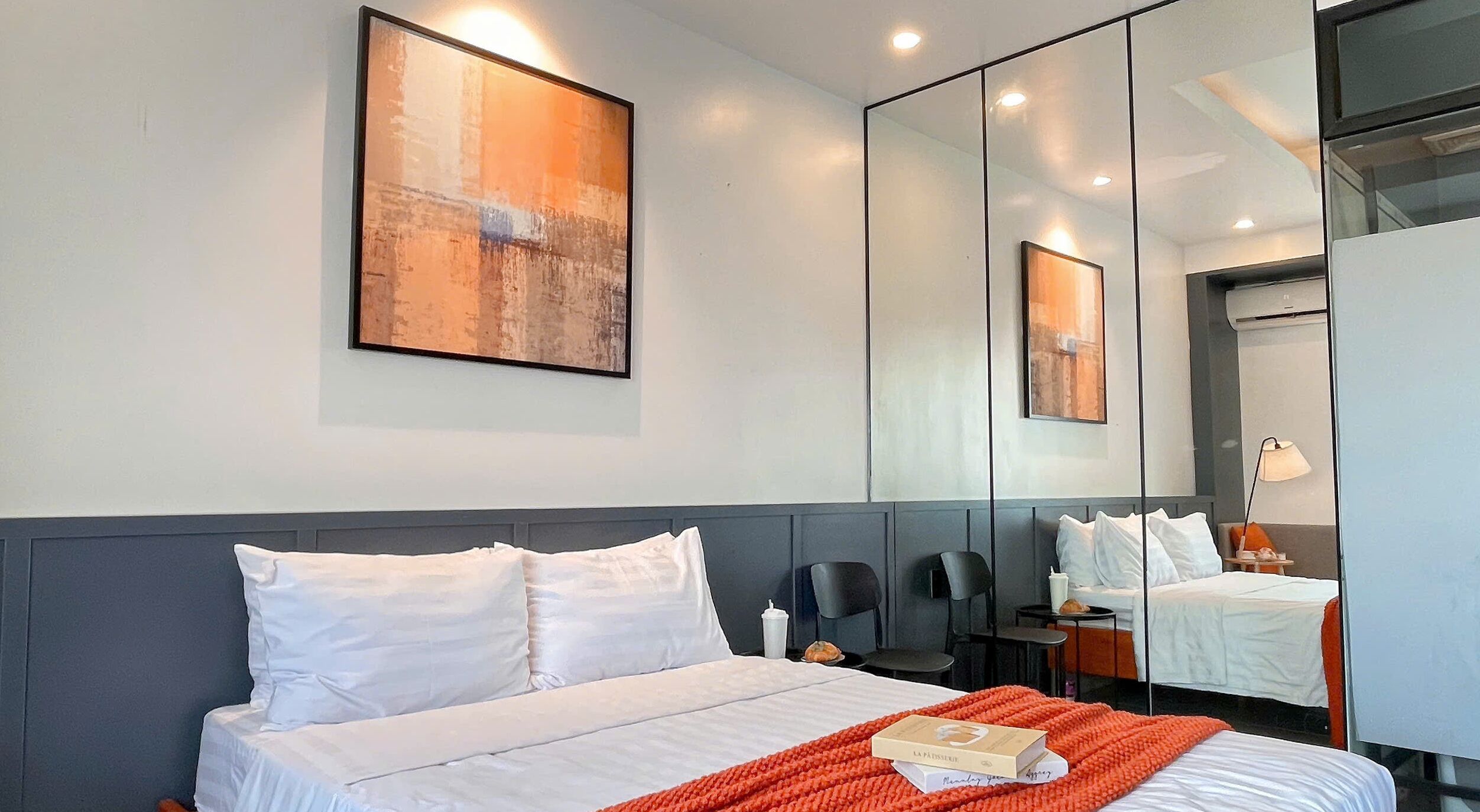 Ein Hotelzimmer mit einem großen Bett, einem Nachttisch, einem Sessel, einem kleinen Tisch mit Lampe und einem großen Spiegel.