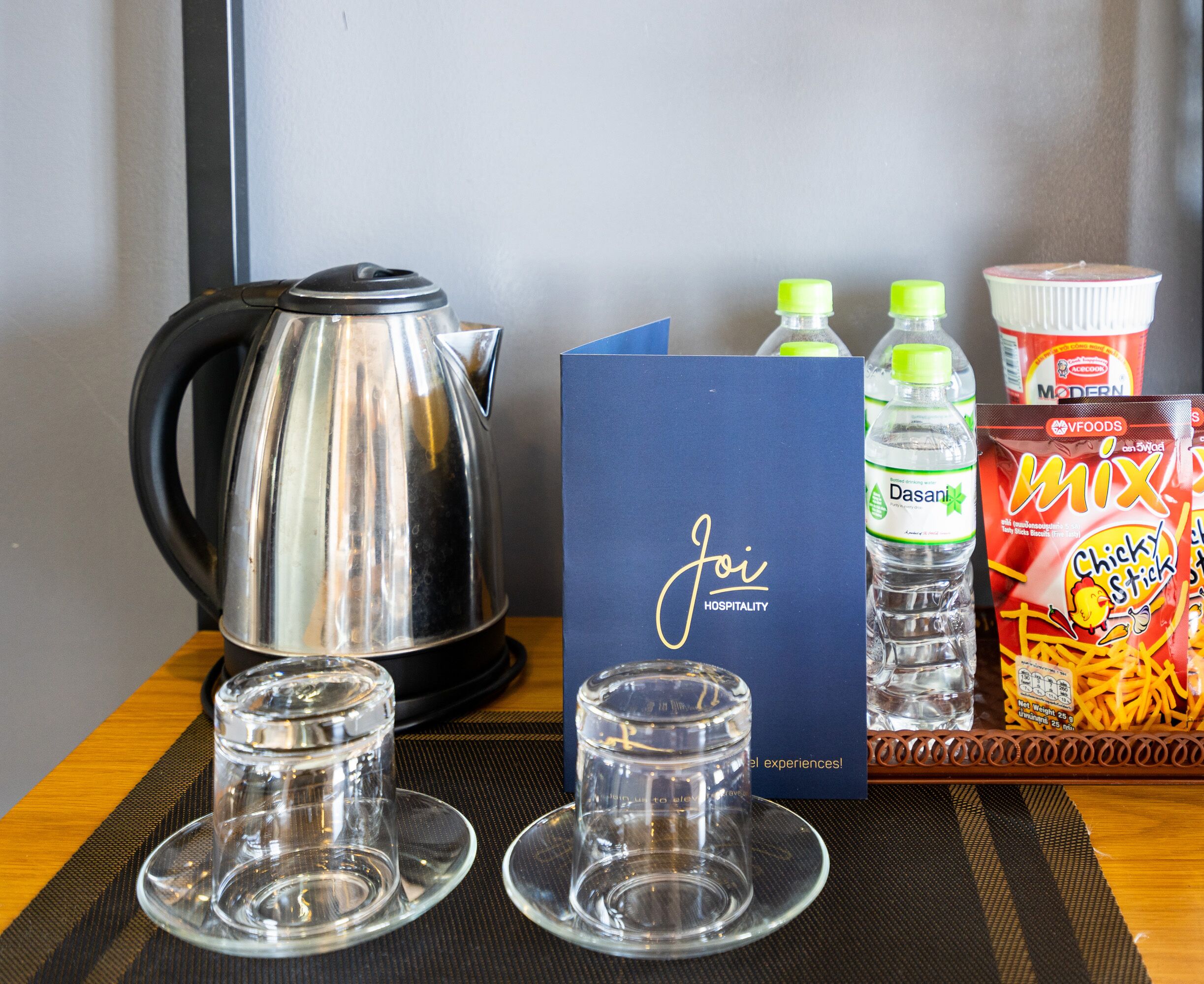 A table with a kettle, two glasses, a water bottle, a box of 'Chicky Stick' fries, and a 'Joi Hospitality' card.