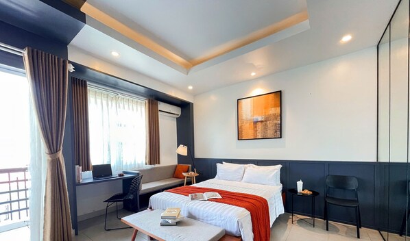 A modern hotel room with a bed, a desk, a chair, a small table, and a window with curtains. - Joi Hospitality - Hoang Anh (Ho Chi Minh City)