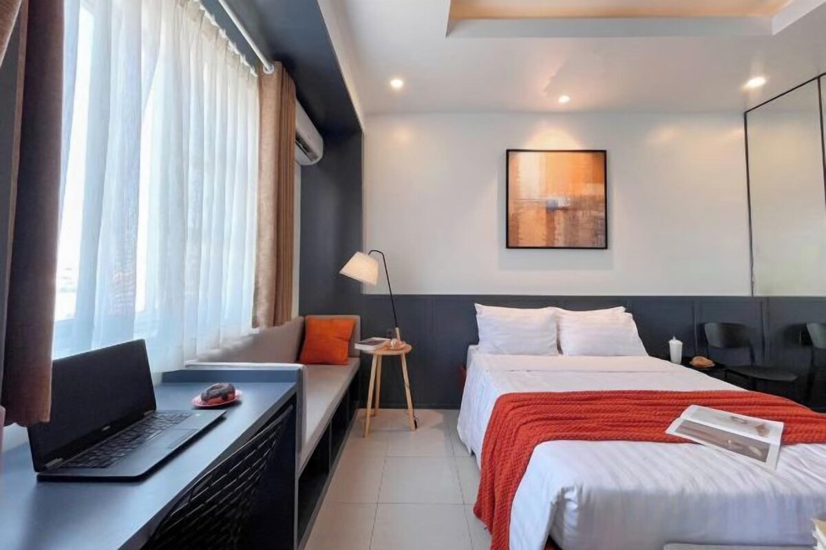 Une chambre d’hôtel moderne équipée d’un lit, d’un bureau avec un ordinateur portable, d’une table de chevet et d’une fenêtre avec des rideaux.