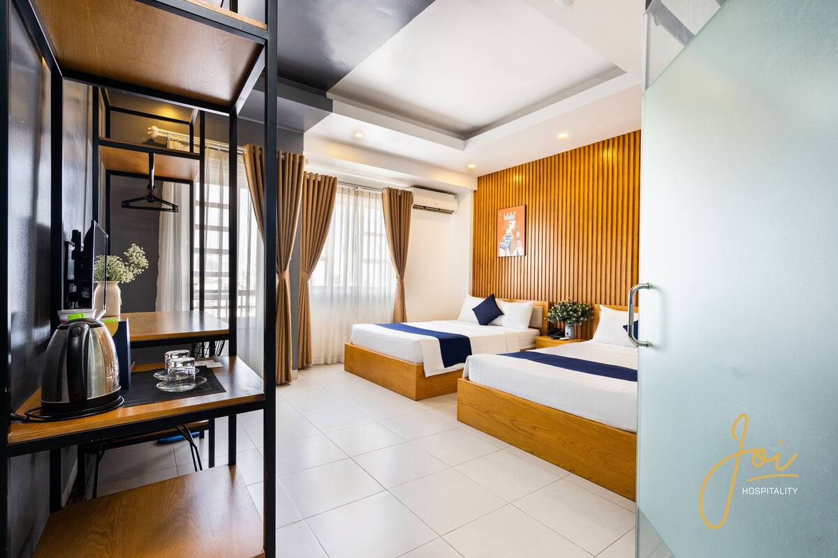 A hotel room with two beds, a wooden desk, a coffee maker, and a wall-mounted TV.