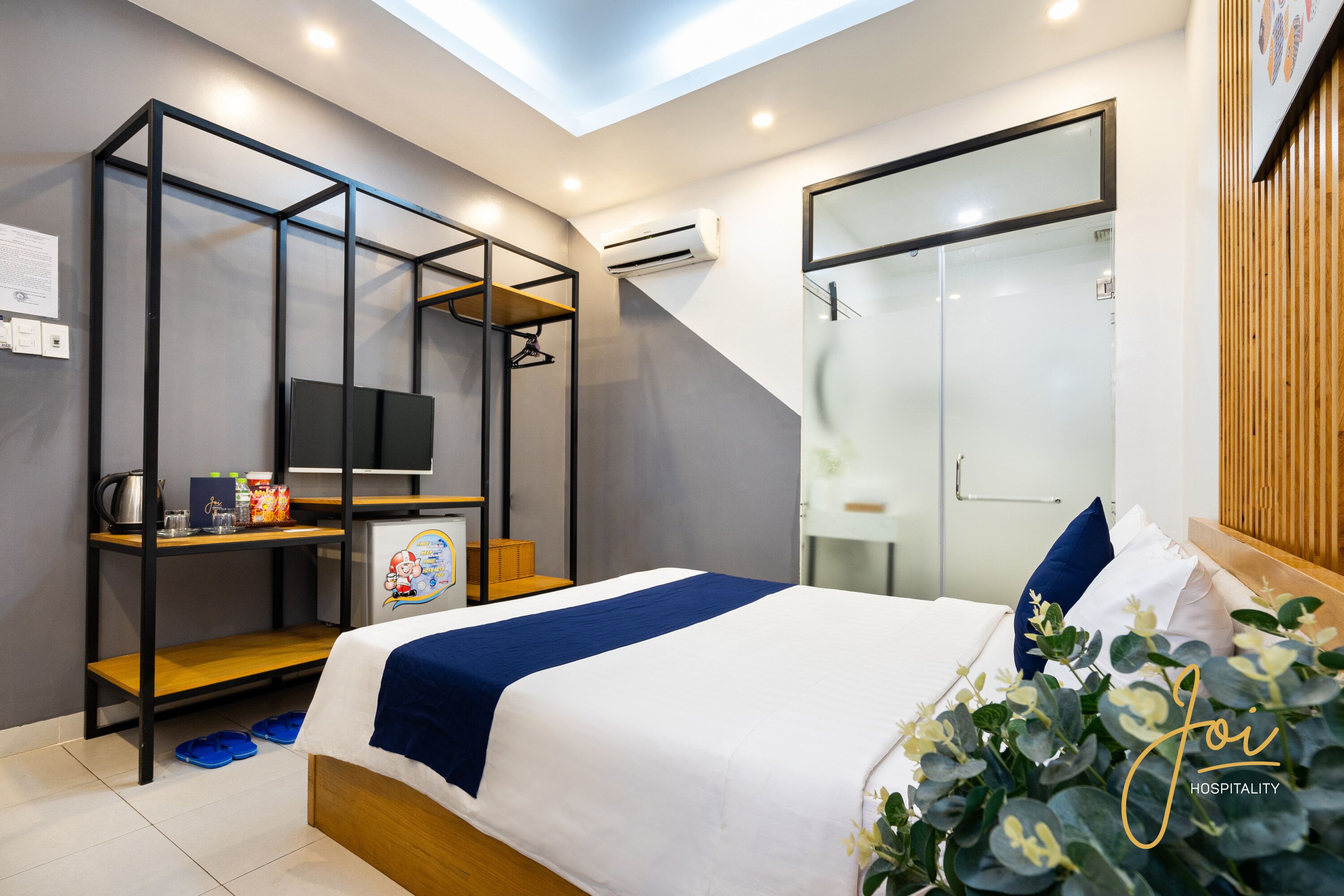 A modern hotel room with a bed, a desk, a TV, and a shower area.