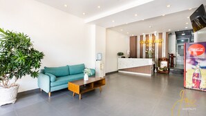 A modern hotel lobby with a teal sofa, a wooden coffee table, a reception desk, and a Coca-Cola refrigerator. - Joi Hospitality - Hoang Anh (Ho Chi Minh City)