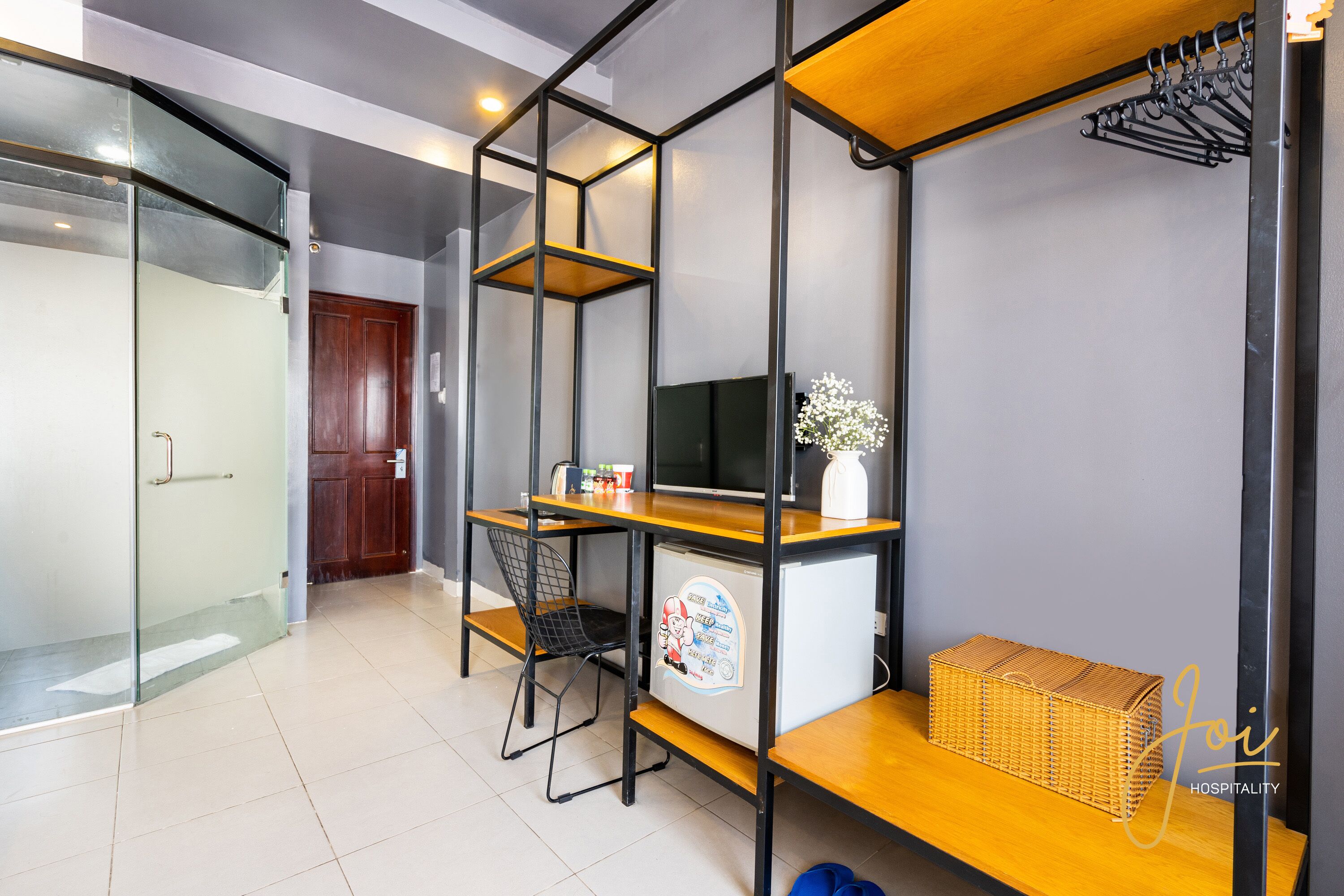 Habitación de hotel pequeña con kitchenette, televisor, un rincón de descanso y una puerta de vidrio que da a la zona de la ducha.