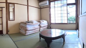 A traditional Japanese room with tatami flooring, a low table, a stack of futons, a wooden ladder, and a large window. - Rakucho Ryokan (Kyoto)