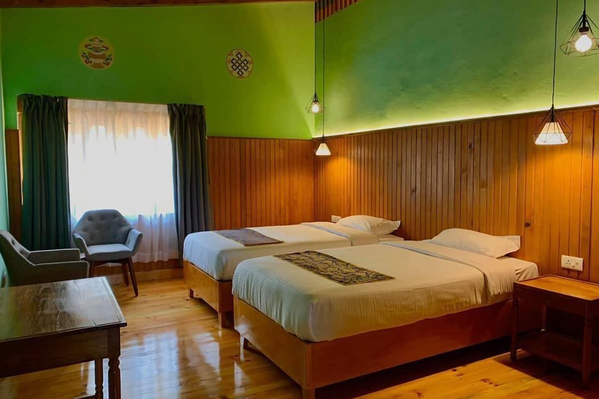 A room with two beds, wooden walls, a green accent wall, a desk, and a chair.
