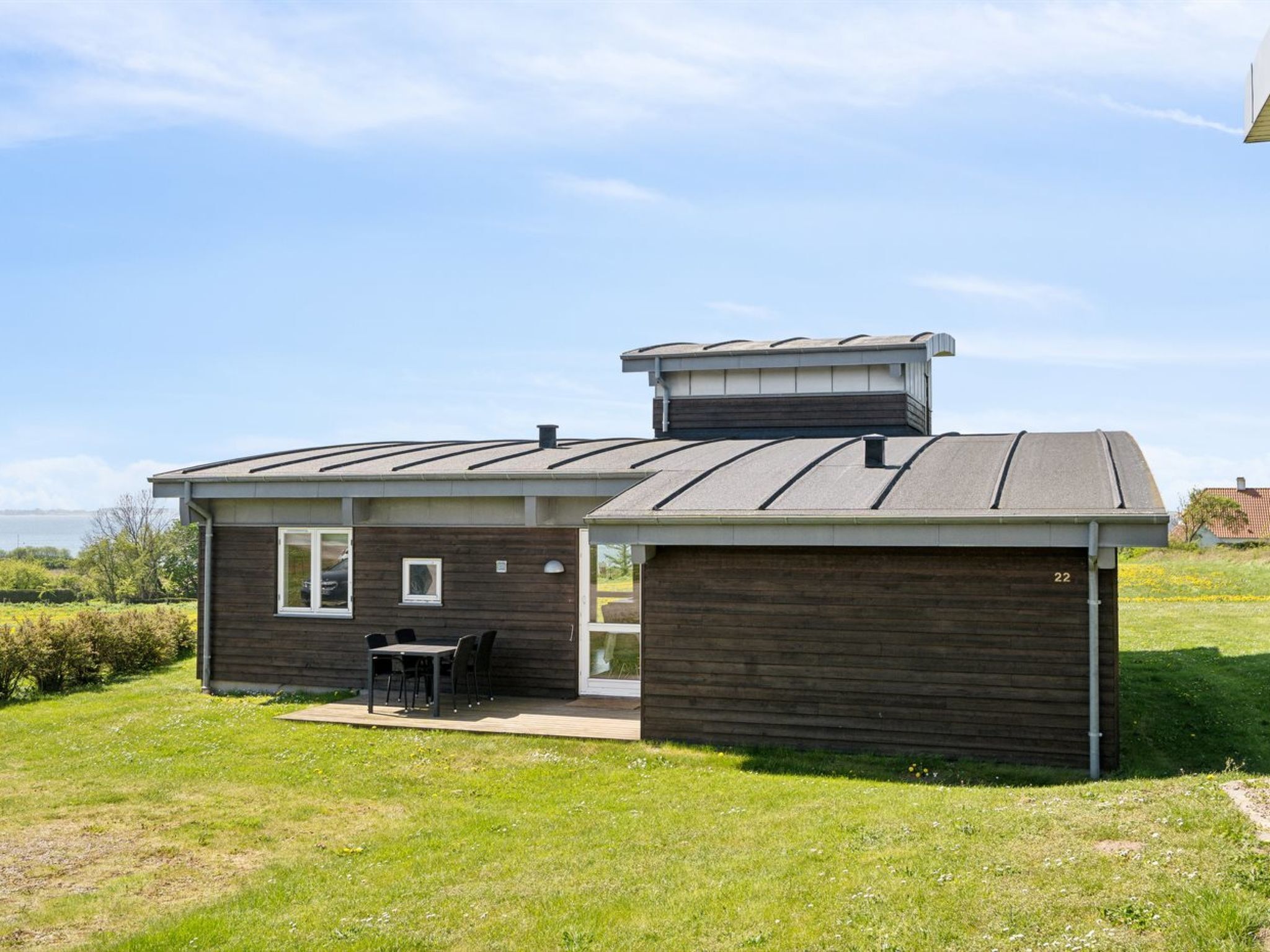 A modern house with a large garage, a patio with outdoor furniture, and a view of the sea.
