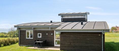 A modern house with a large garage, a patio with outdoor furniture, and a view of the sea.
