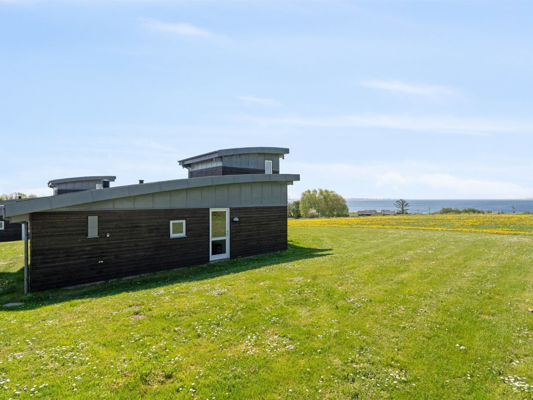 A modern building with a flat roof and a small door, surrounded by a grassy field and a body of water in the background.