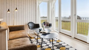 A cozy room with a wooden ceiling, a brown sofa, a small round table with a book and glasses, and a view of a grassy field through large glass doors. - "Halvor" - 275m from the sea by Interhome (Faaborg)