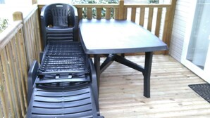 A deck with a black lounge chair and a table.