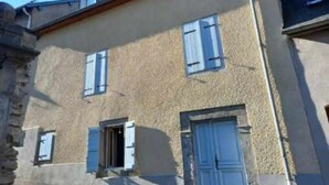 A two-story building with a textured facade, multiple windows with shutters, and a visible door. - Maison de Village (Viella)