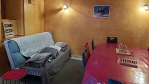 A cozy room with a wooden ceiling, a sofa with a blanket, a small table with a keyboard, and a framed picture on the wall. - Maison de Village (Viella)