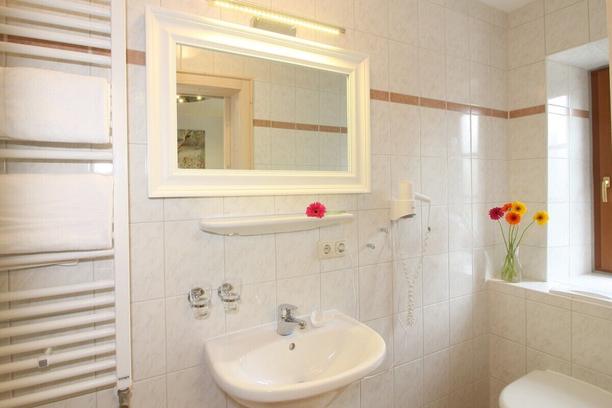 A bathroom with a white sink, a mirror, a towel rack, and a window with flowers.