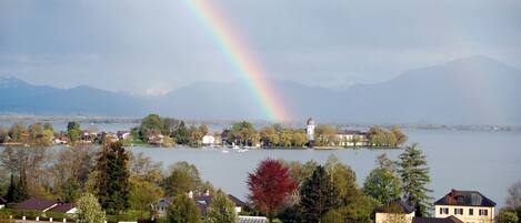A lakeside view with houses, a lighthouse, and mountains in the background.