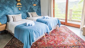 A bedroom with two beds, a large window, and a view of greenery.