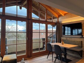 A room with large windows, a wooden ceiling, a table with chairs, and a bench. - Ferienwohnung Bergblick 55 qm, mit Blick auf den Chiemsee (Rimsting)