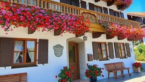 Ein traditionelles Chalet mit Balkonen, die mit bunten Blumen, hölzernen Bänken und einem Schild als Pension gekennzeichnet sind.