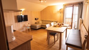 Une pièce chaleureuse et bien éclairée, avec un décor intérieur en bois, un canapé, une table à manger et un téléviseur fixé au mur.