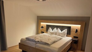 Une chambre à coucher moderne avec une tête de lit en bois, un lit recouvert de linge de maison blanc et une table de chevet.