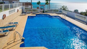 A swimming pool with a view of the ocean, surrounded by a white fence and palm trees.