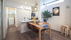 A modern kitchen with a built-in refrigerator, a dining area with a wooden table and chairs, and a large potted plant. - Travel time Koji Higashi 4LDK Max8ppl (Osaka)