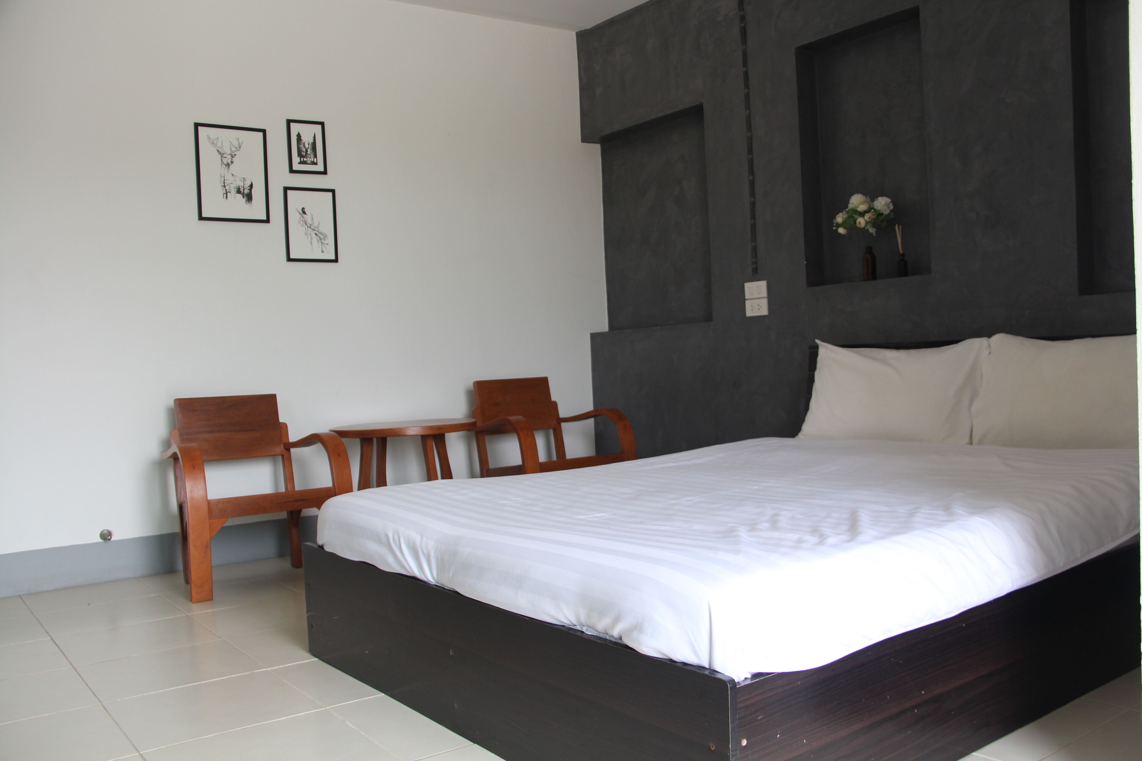 A bedroom with a large bed, two wooden chairs, a small table, and three framed pictures on the wall.