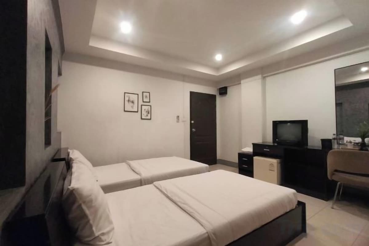 A bedroom with two beds, a desk, a chair, a TV, and a wardrobe.