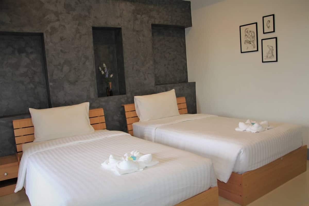 Quarto de hotel com duas camas, cabeceiras de madeira e parede cinza com textura.