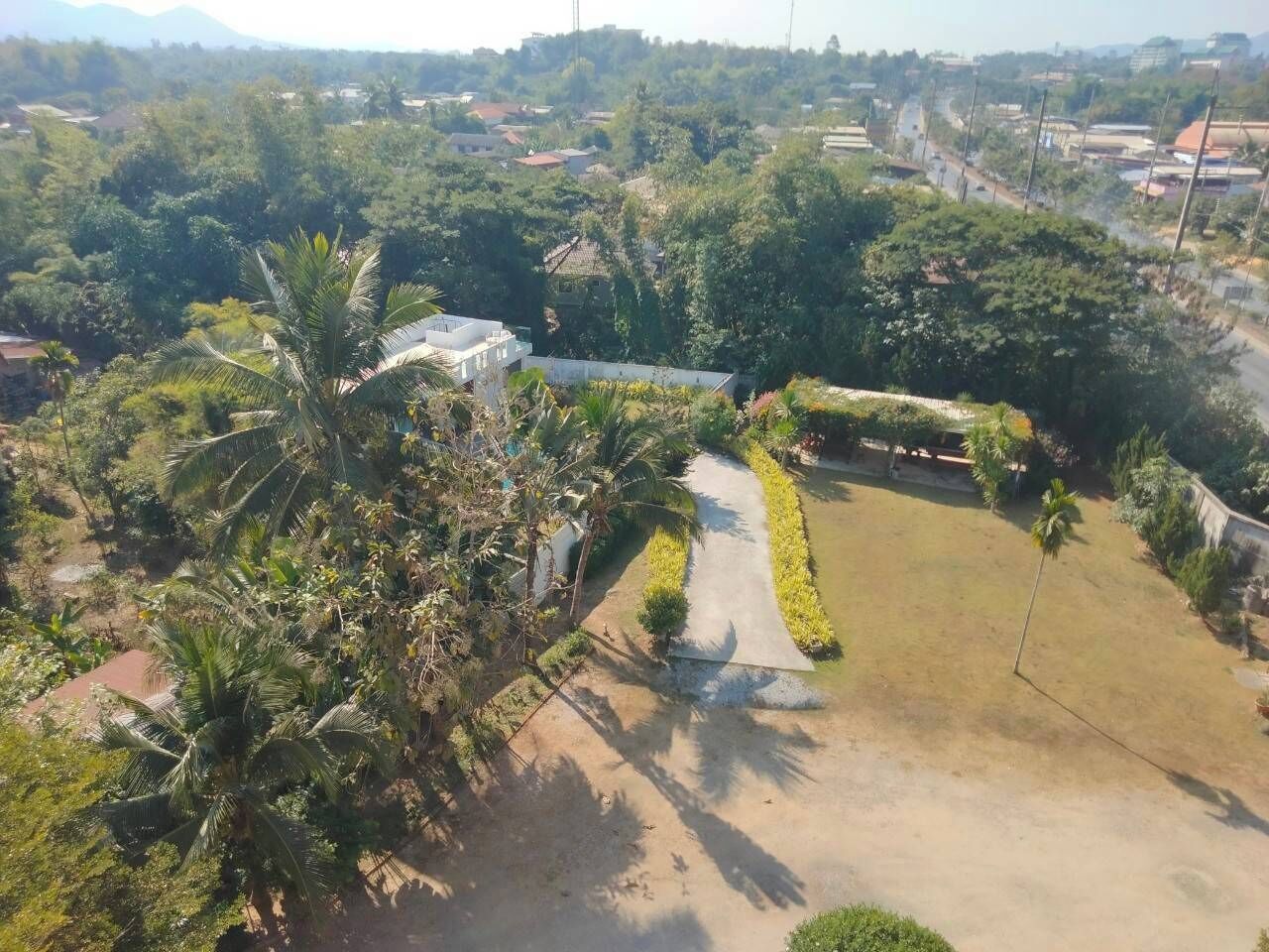 Vista aérea de un área residencial con un camino pavimentado que conduce a una casa rodeada de abundante vegetación y palmeras.