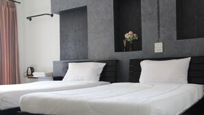 A hotel room with two single beds, a small table with a kettle, and a wall-mounted shelf with flowers. - Pilatus Apartment (Mueang Loei)