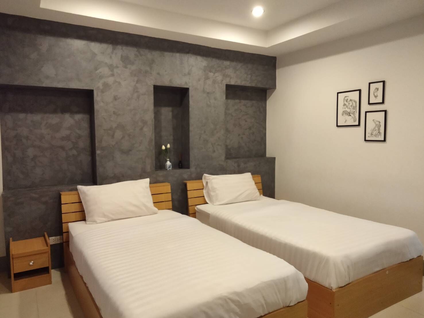 A modern bedroom with two single beds, a small bedside table, a nightstand, and a wall-mounted shelf with a vase.