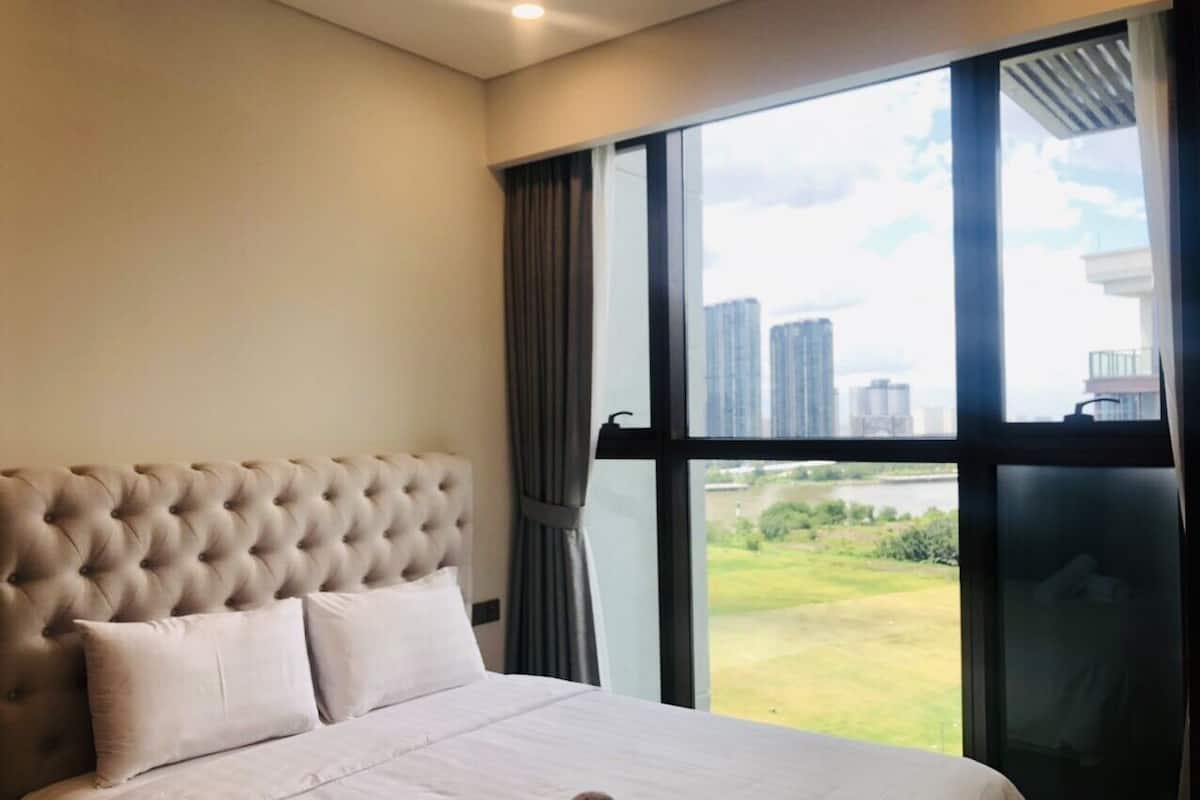 A bedroom with a large bed, a tufted headboard, and a view of a cityscape through a large window.