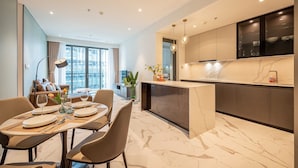 Une cuisine moderne avec un plan de travail en marbre, un coin repas avec une table dressée pour quatre personnes et une vue sur la ville grâce à de grandes fenêtres.