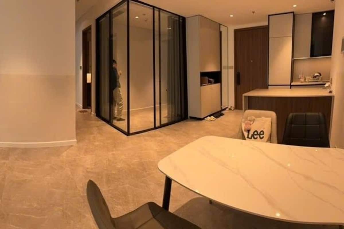 A modern living room with a sofa, a TV, and a glass partition separating the living area from a kitchen.