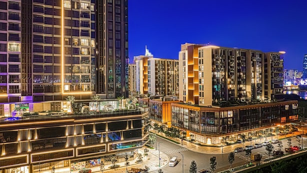 Un quartier urbain moderne, avec de hauts immeubles, un carrefour bien éclairé et une promenade piétonne.