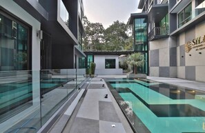 A modern building with a glass-enclosed swimming pool and a small garden area. - B405 -1 Bedroom Condo Pool View Near Ao Nang Beach (Krabi)