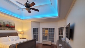 Ein Schlafzimmer mit einem Bett, einem Deckenventilator, einem Gemälde, einem Nachttisch, einem Schreibtisch und einem Fernseher.