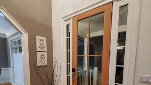 Ein Korridor mit Holzdielen, einer braunen Tür mit Glasfeldern und einer schwarzen Fußmatte.