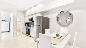 A modern kitchen with white cabinets, stainless steel appliances, and a dining area with a table set for two. - Siesta Key Village, Pool, Beach Access 4-min. Walk, 1bdr (Siesta Key)