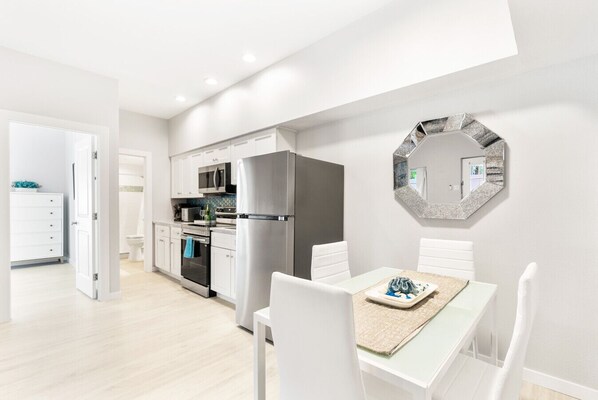 A modern kitchen with white cabinets, stainless steel appliances, and a dining area with a table set for two. - Siesta Key Village, Pool, Beach Access 4-min. Walk, 1bdr (Siesta Key)